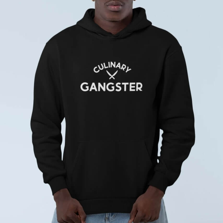 A man wearing a black hoodie with a custom design of two knives and the words "Culinary gangster."