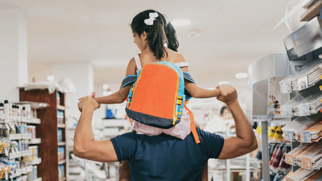 How big is back to school spending A man carries a child on his shoulders while shopping in a store with a backpack on.