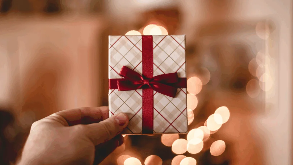 A person holding a gift card wrapped in colorful paper and tied with a bright red bow.