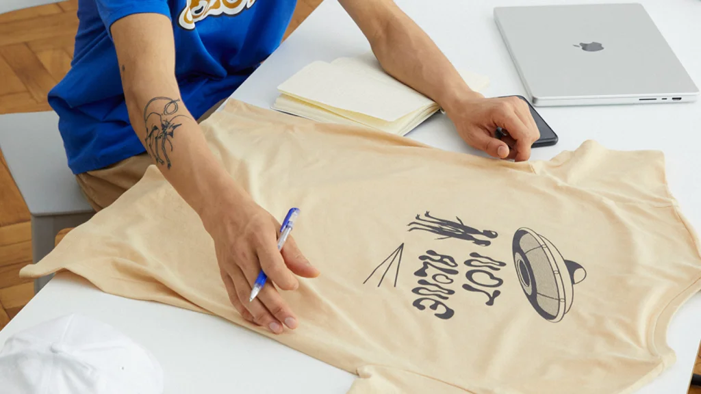 A man in a shirt sits at a table, working on a laptop. The setting is casual and focused on his task.