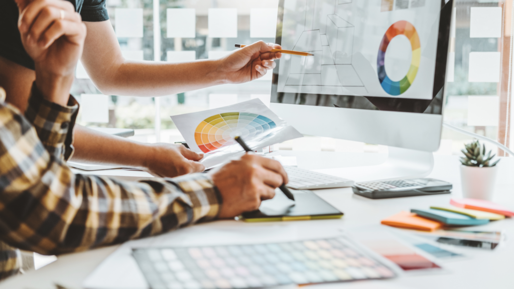 A man and woman collaborate on a computer, analyzing a color chart for a project.