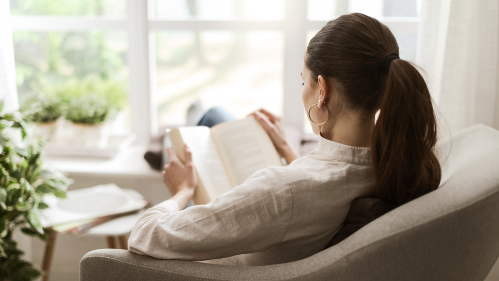A woman sits in a chair, engrossed in reading a book, surrounded by a cozy atmosphere.