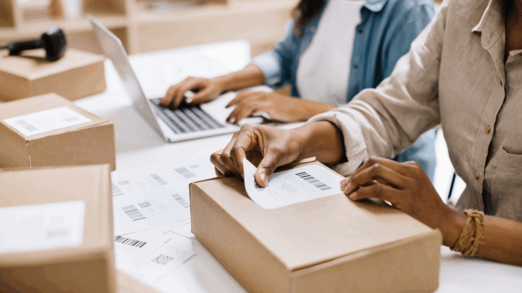 Two individuals collaborating on a laptop beside an open box, focused on their work.