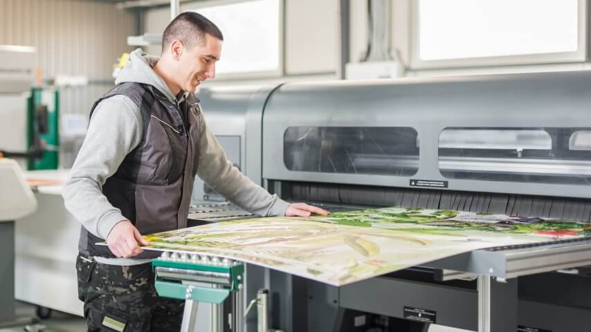 A man operating a machine that prints large art posters.