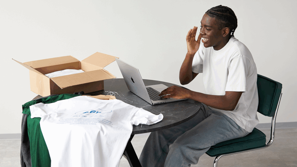A man seated at a table, working on a laptop with a box beside him.