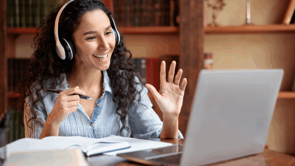 Online courses and online tutoring services A smiling woman is wearing headphones and teaching online using a laptop.