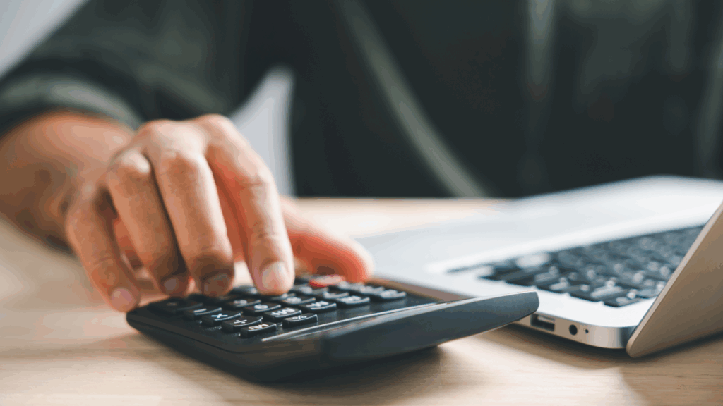 A person calculates on a desk with a calculator, alongside a laptop, focused on their work.