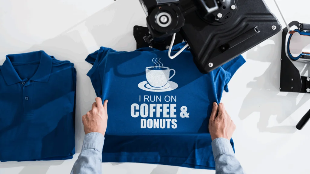 A person holds a blue t-shirt featuring the words "Coffee" and "Donuts" printed on the front.