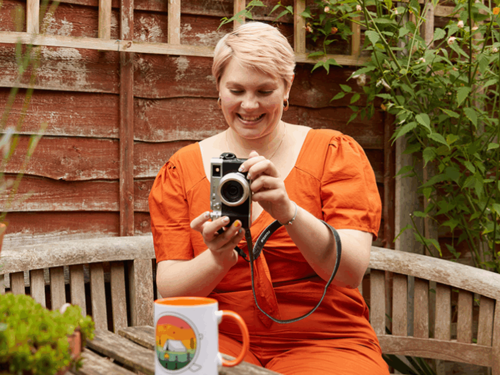 Print on Demand A smiling young woman is taking a picture of a mug made with print-on-demand as a low-cost business idea.