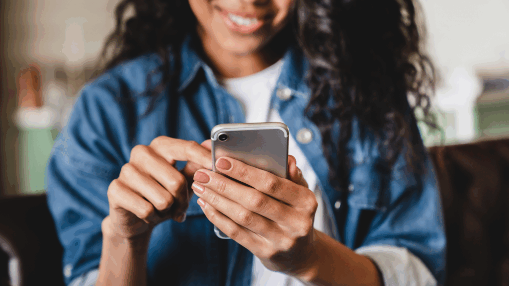 Social media management services A smiling woman is using a mobile phone that she’s holding in her hands.