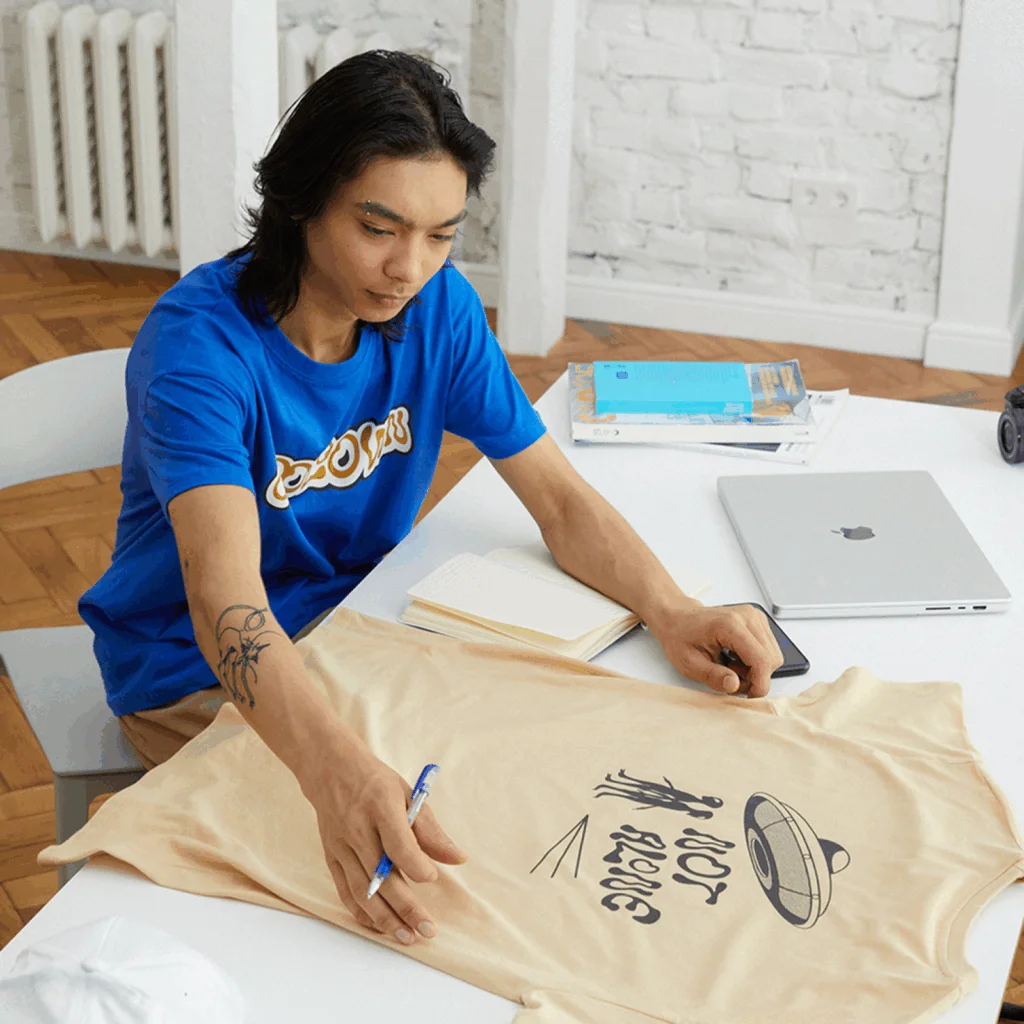 A young man is looking at a t-shirt placed on a table.