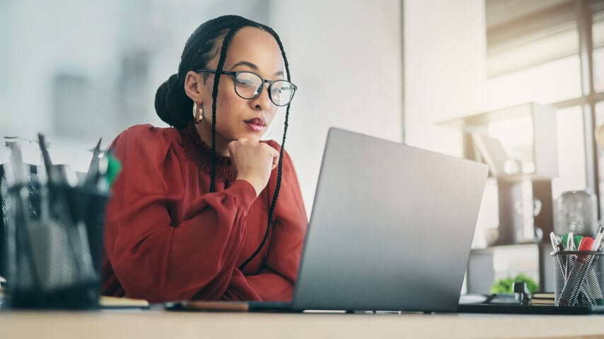 Various business models for selling without inventory A woman with glasses wearing a red blouse, sitting in front of a laptop and looking at the screen.