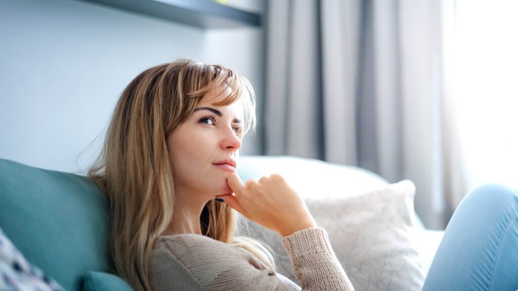 A woman looking to the side, holding her hand below the chin and thinking.
