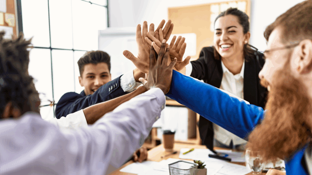 Business professionals in an office celebrating with hands raised in the air, expressing success and teamwork.