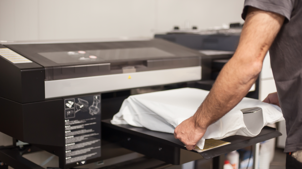 A person prepares a white t-shirt on a tray for printing in a digital garment printer.