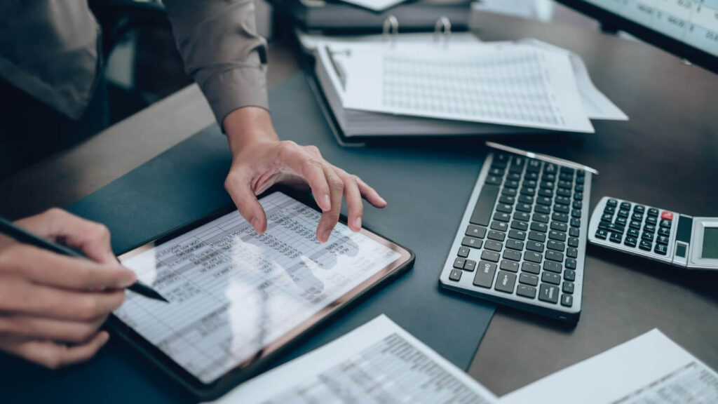 A tablet on top of a table with an open file with cost calculations.
