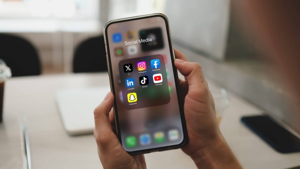 A close up shot of a mobile phone in hands with various social media apps on the screen.