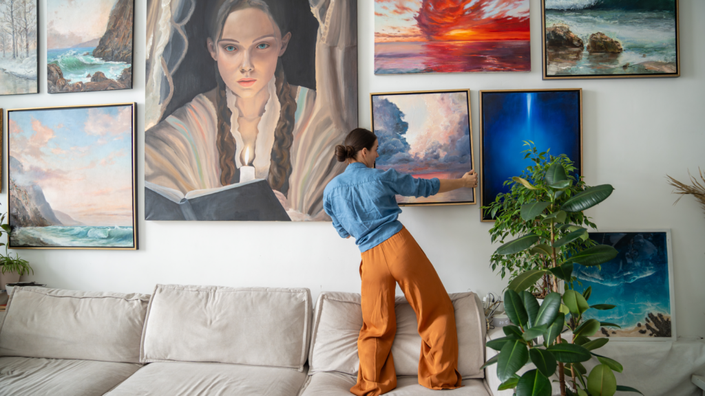 Stock photos and digital art A woman hanging a painting on a wall full of paintings.
