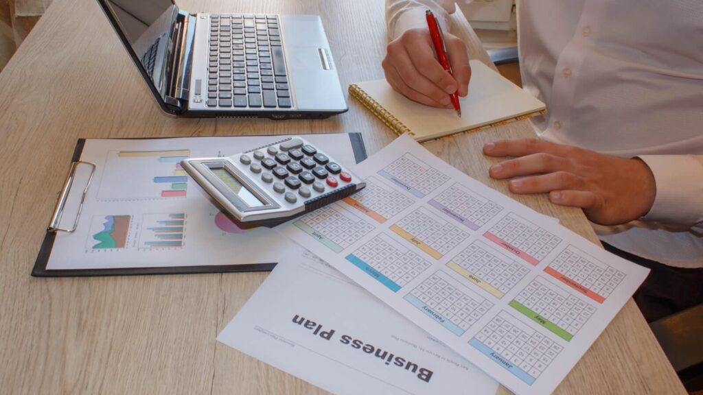 Write a business plan A person sitting at the table, writing in a notebook.