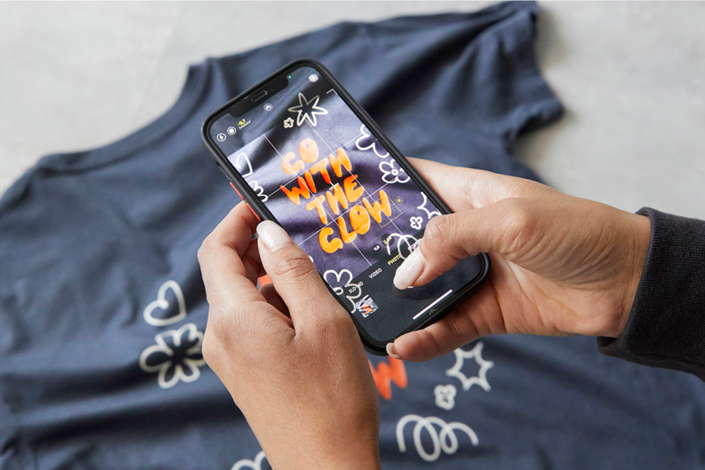 How to create a t shirt design Printify A person takes a photo of a t-shirt design that says "Go with the glow."