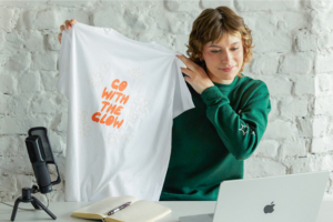 A woman holding up a white print-on-demand t-shirt.