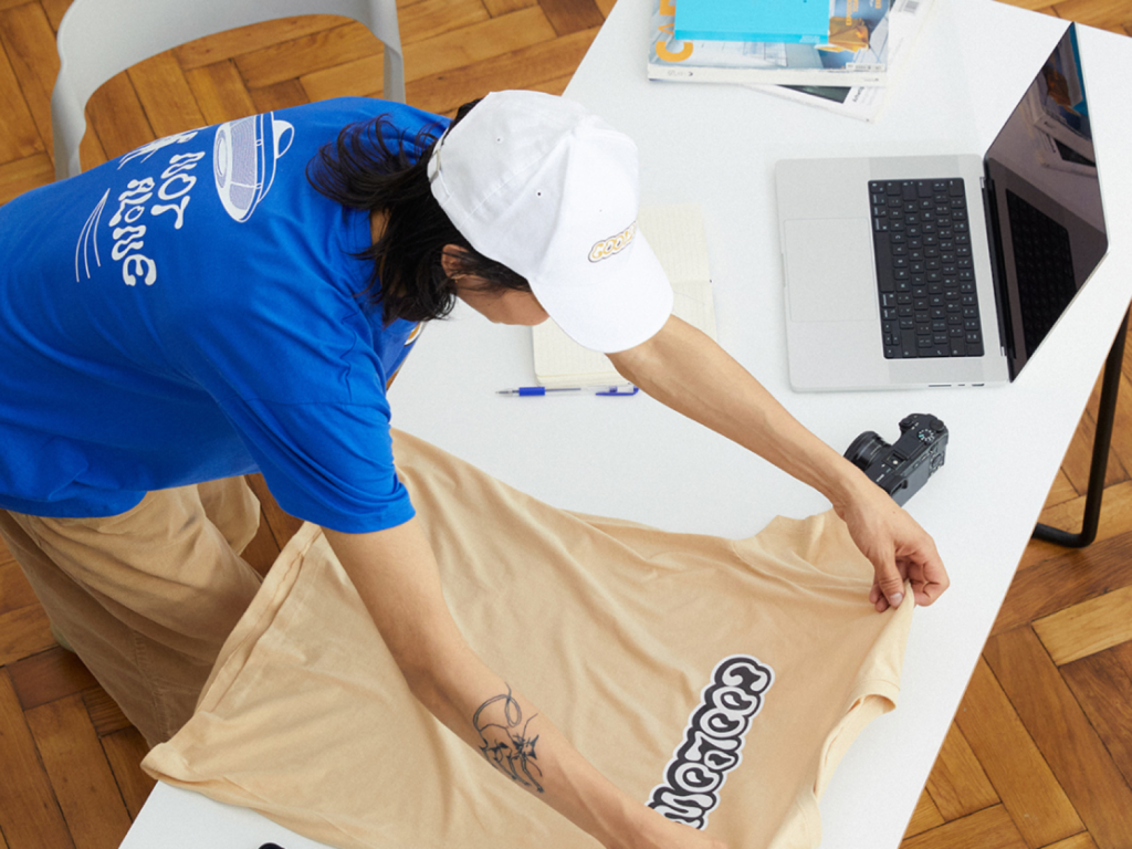A person laying out a custom t-shirt on a table to take a picture of it.