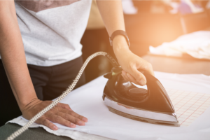 A person ironing a t-shirt, applying heat to transfer a design from transfer paper onto the fabric.