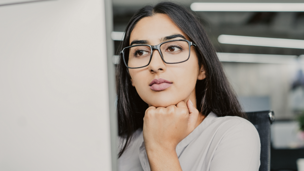 A dark-haired woman in glasses looking at a screen.