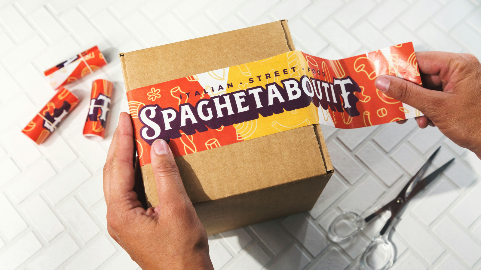 Create your sticker designs A person sticking a “Spaghetaboutit” sticker on a cardboard box.