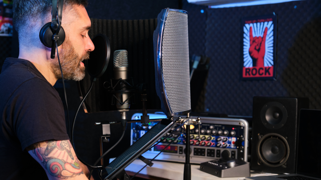 A man holds a microphone while seated in front of a computer, engaged in a voice recording session.