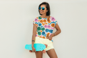A woman in a vibrant all-over-print shirt and shorts, confidently holding her skateboard.