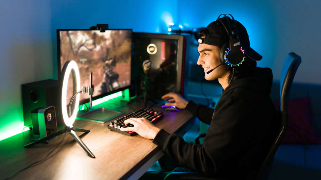 How to make money playing video games. A man wearing a black shirt and headphones is focused on playing a video game on his computer.