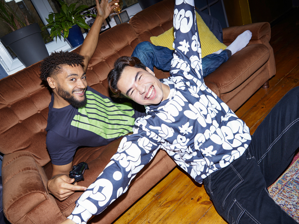 Two guys sitting on the couch playing video games wearing custom merch.