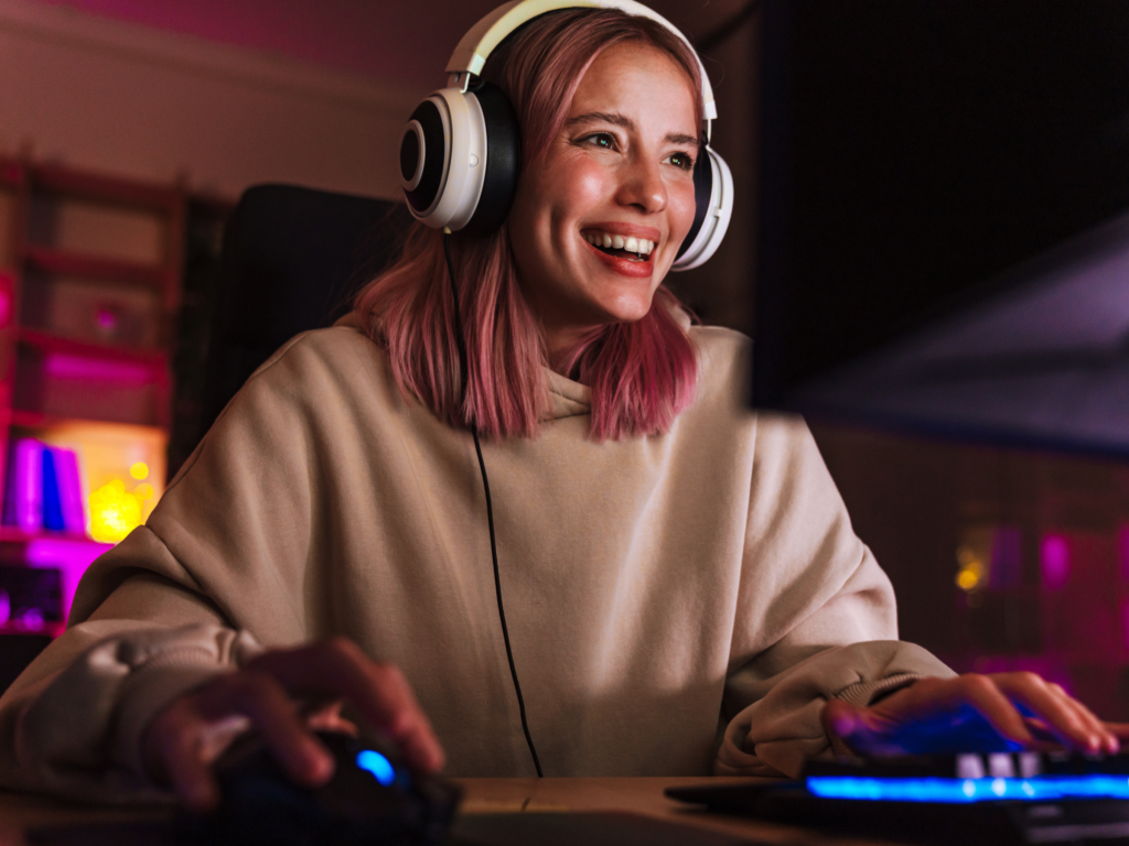 A woman is playing video games, wearing headphones and beige hoodie.
