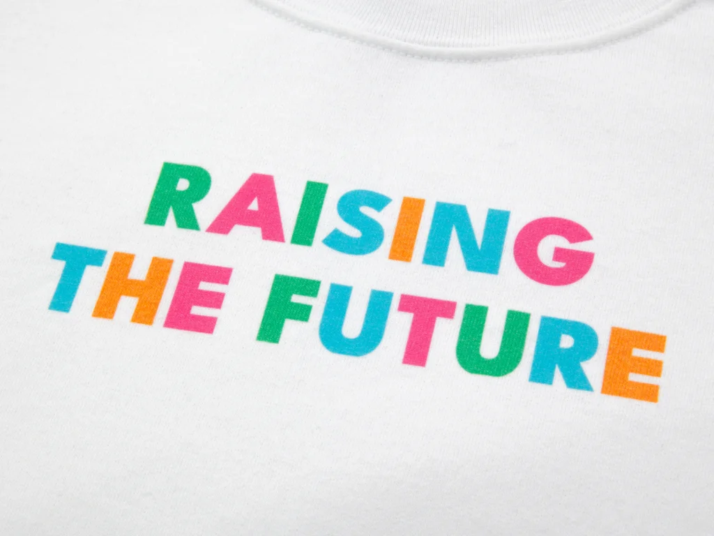 Bold, multi-colored text reading "Raising the Future" is printed on a white t-shirt.