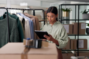 A woman examines a tablet while shopping for clothes in a retail store.