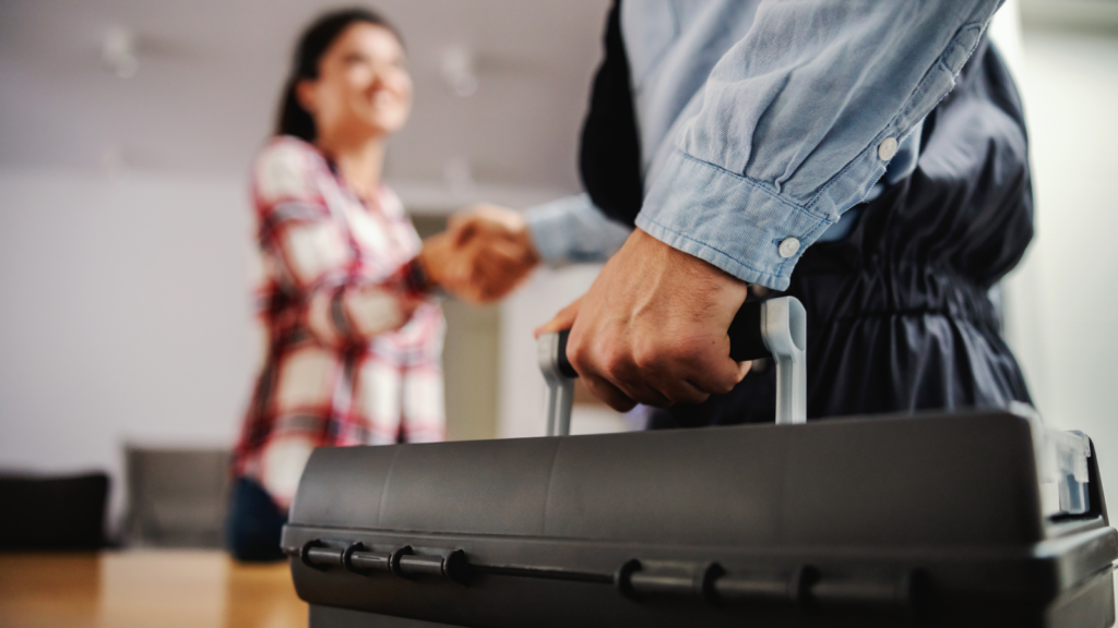 A blurred silhouette of a woman in a plaid shirt shakes hands with a handyman holding a toolbox.