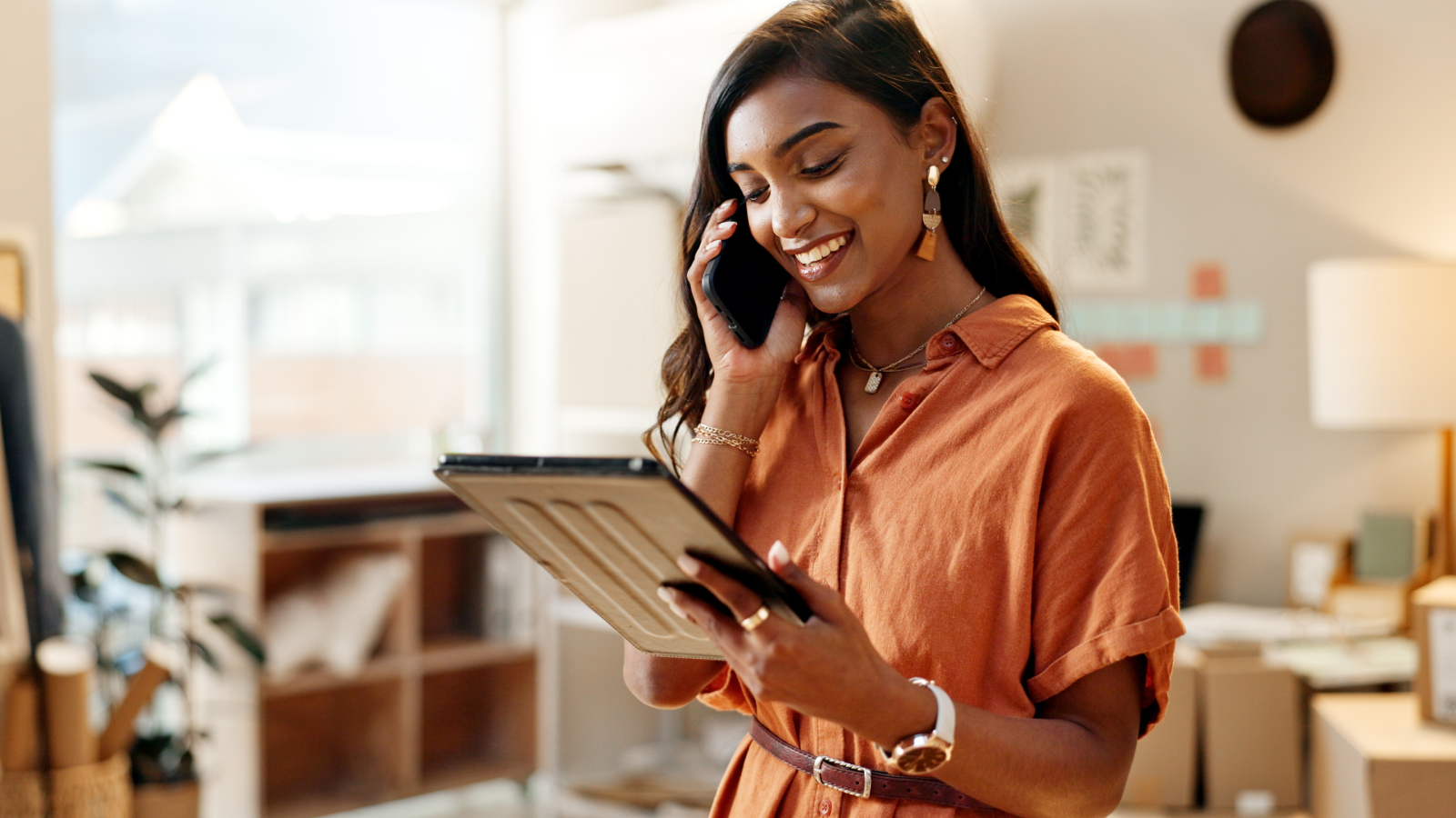 A woman stands in a room, holding a tablet in her hands, looking focused and engaged with the device.