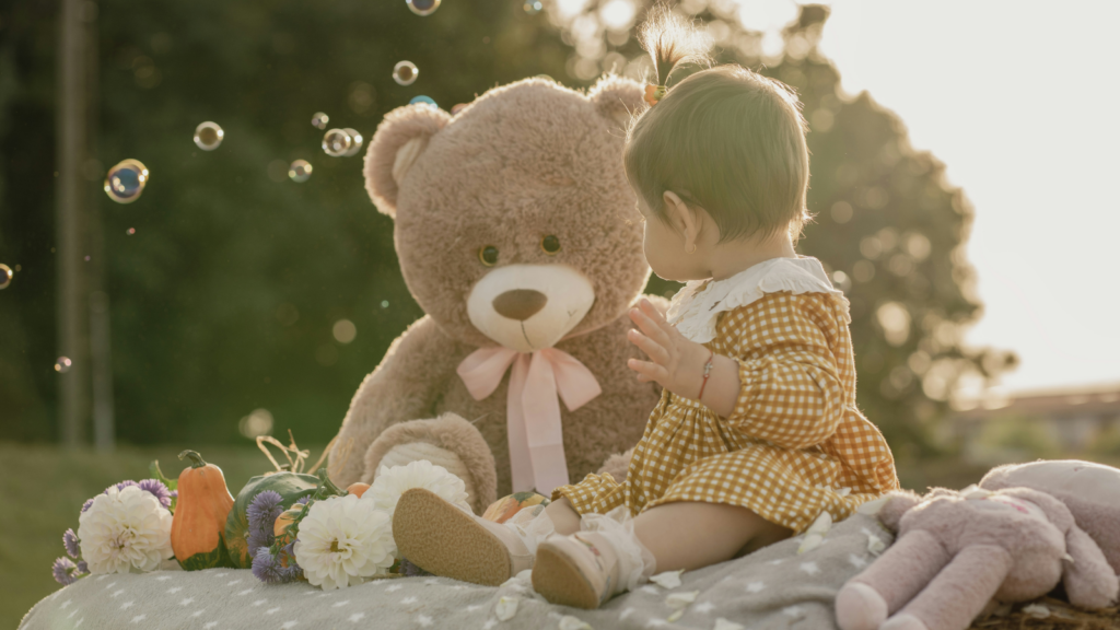 Baby products Dropshipping business ideas A baby girl seated on a blanket, with a teddy bear resting next to her.