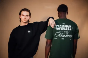 Two men stand side by side, both wearing green t-shirts, smiling at the camera in a casual outdoor setting.