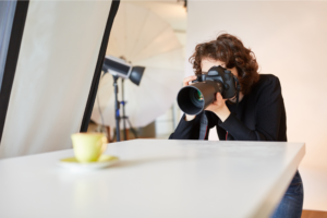 A woman photographer holding a DSLR camera and taking a picture of a product.