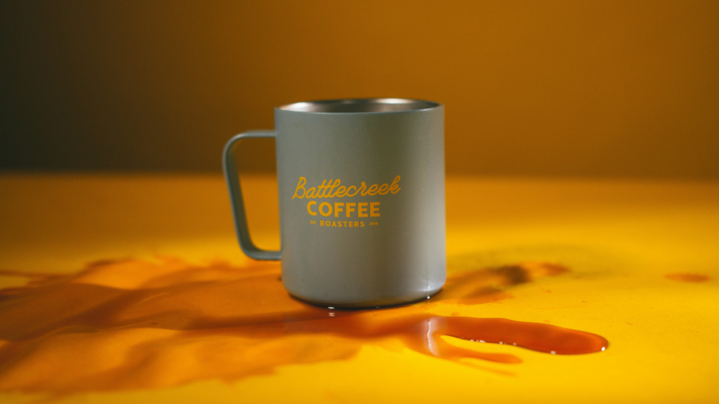 Mugs and tumblers Conference swag A coffee mug is placed on a table, featuring a splash of orange liquid around it.