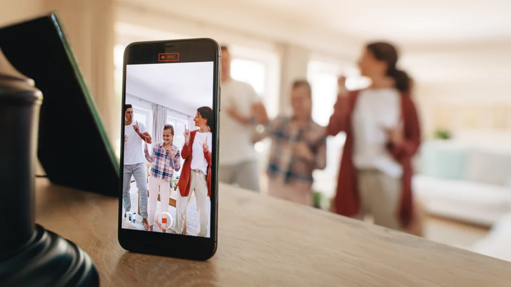 A smartphone on a table records a family cheerfully dancing in a bright living room.
