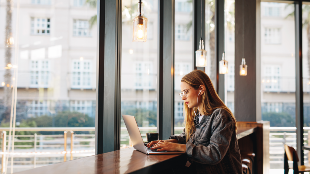 Print on Demand Side hustles for introverts A woman at a table using a laptop, showcasing concentration in a warm and inviting workspace.