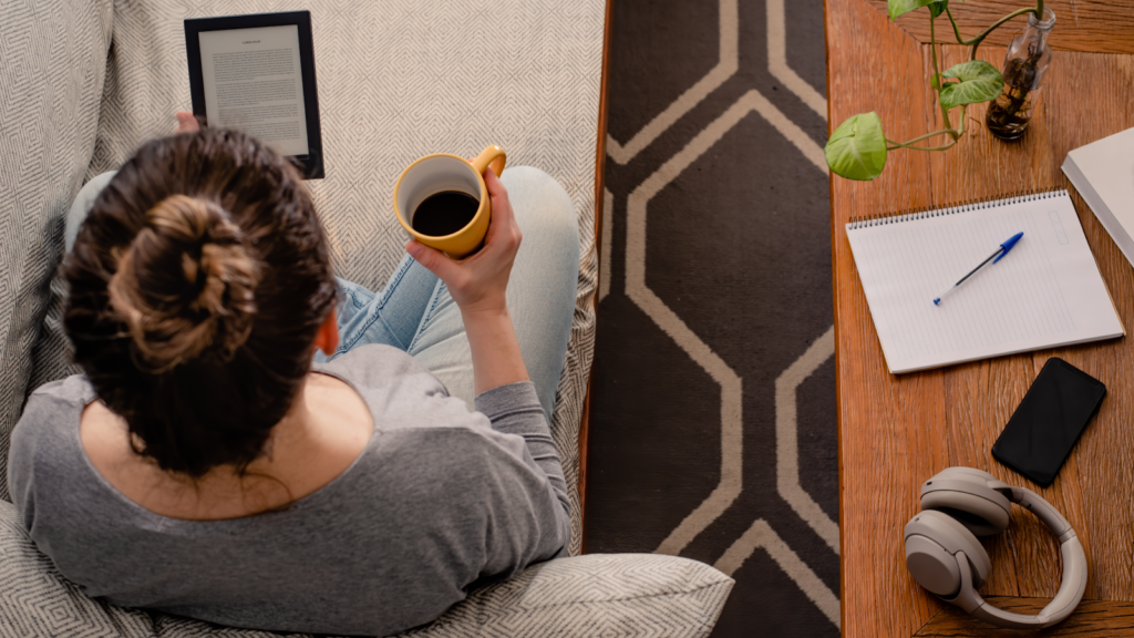 Publish eBooks Side hustles for introverts A woman using a tablet and sipping from a coffee mug, seated comfortably at a table.