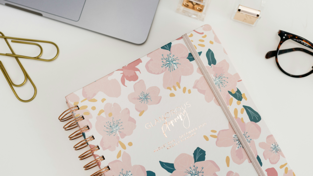 Start a new stationery business and join a big buck industry A floral-designed planner in pink next to a notebook with a gold frame, highlighting a chic and organized workspace.