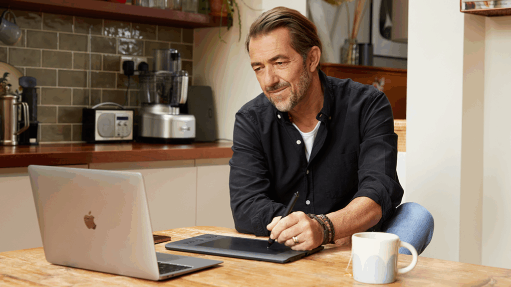 Affiliate marketing Passive income for artists A man sitting in a kitchen and working using a laptop and a pad.