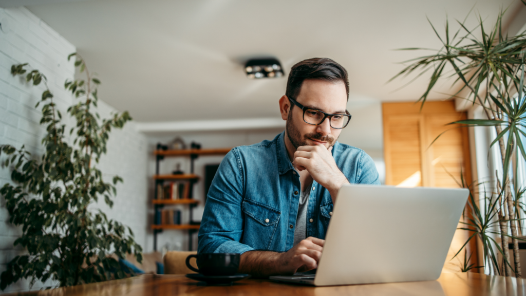 Become an affiliate marketer How to make money as an influencer A man in a blue jeans shirt, sitting at a table and using a laptop.