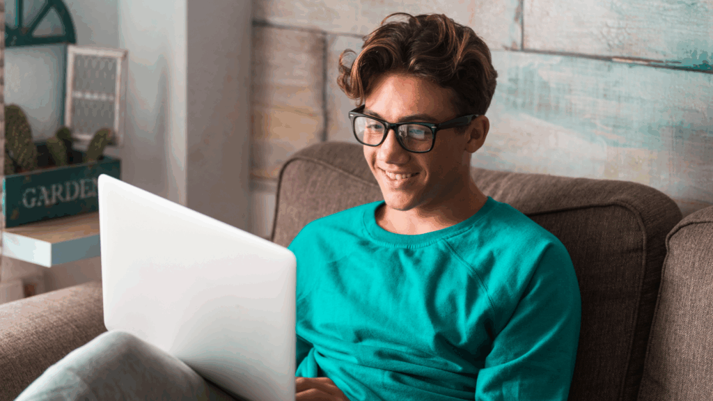 Business tips for teens A smiling young man searching for the best business ideas for teens using a laptop.