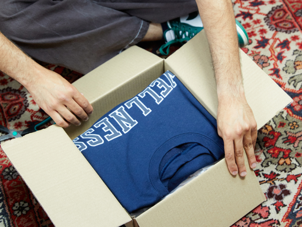 Clothing shoes and jewelry What to sell on Amazon A person unpacking a delivery box with a blue hoodie inside.